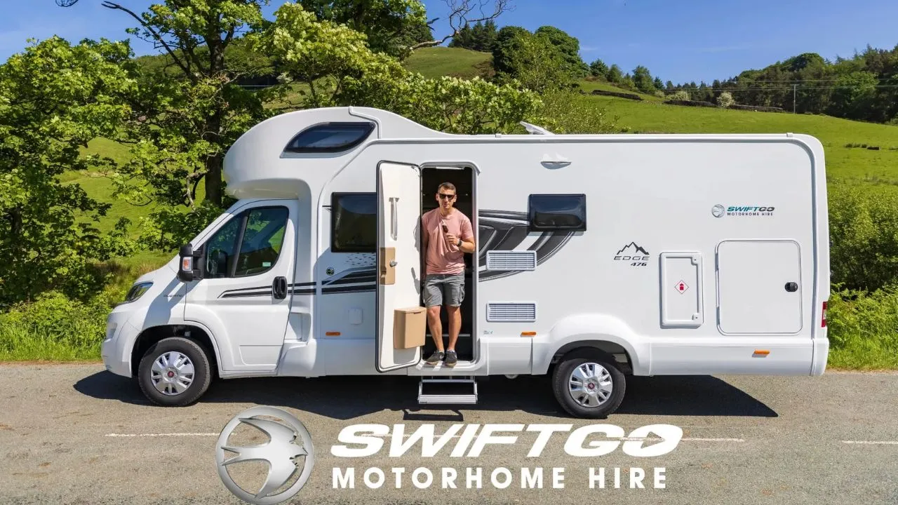 White Swift Go motorhome parked on a rural road with a green landscape in the background and a man stepping out of the door holding a bag.